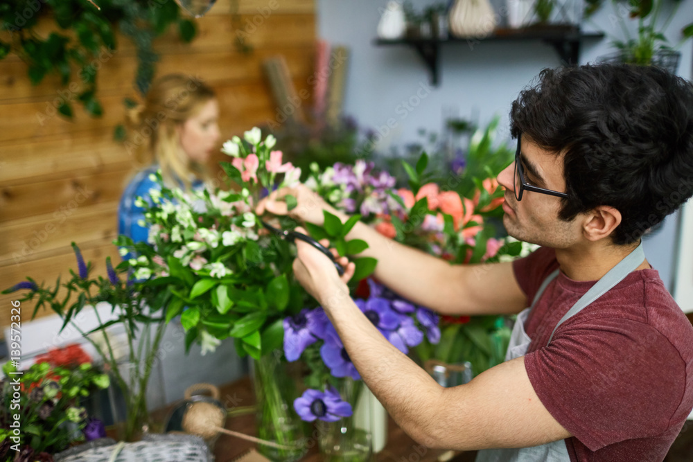 Young man cutting dry leaves while arranging floral bouquets