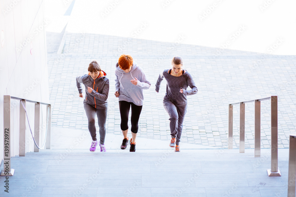 Front view of the group of three athletic women running up stairs during cardio - interval training. Front view of the group of three athletic women running up stairs during cardio - interval training.