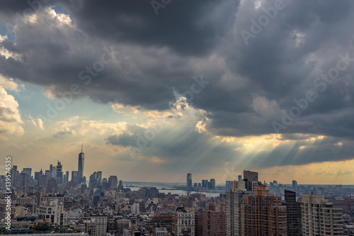 Moody sky over downtown New York City, sun rays through the clouds, view from a rooftop in midtown