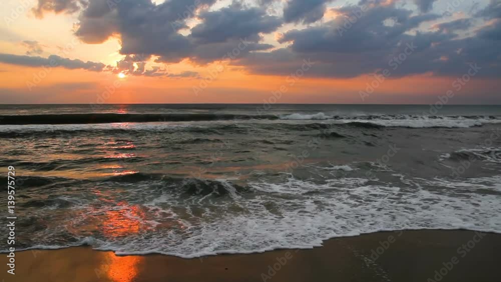 30 second loop features a colorful, cloudy sunrise sky reflected upon the Atlantic Ocean surf and wet beach sand at Nags Head, North Carolina, a popular vacation location on America's East Coast.