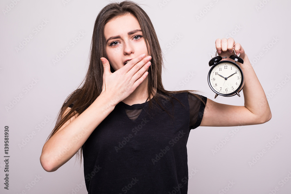 young smiling woman with alarm clock isolated white grey wall ...