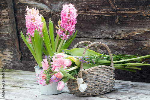 Fototapeta Naklejka Na Ścianę i Meble -  Pinke Hyazinthe mit rosa Frühlingsstrauß in einem Weidenkorb vor verwitterter Holztür