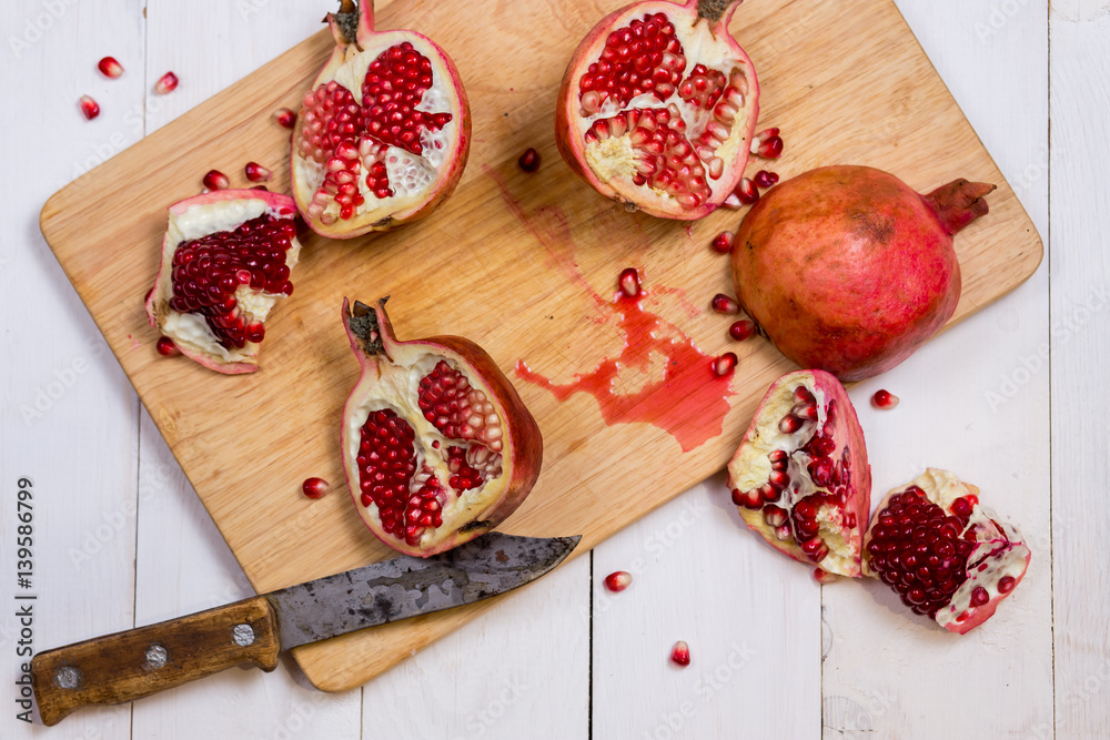 pieces sliced pomegranate on a cutting Board with the old knife on a white wooden background close-up pieces sliced pomegranate on a cutting Board with the old knife on a white wooden background close-up