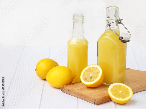 Freshly squeezed lemon juice in bottle and lemons on light background. For vitamin drink or cocktail. Selective focus. Space for text