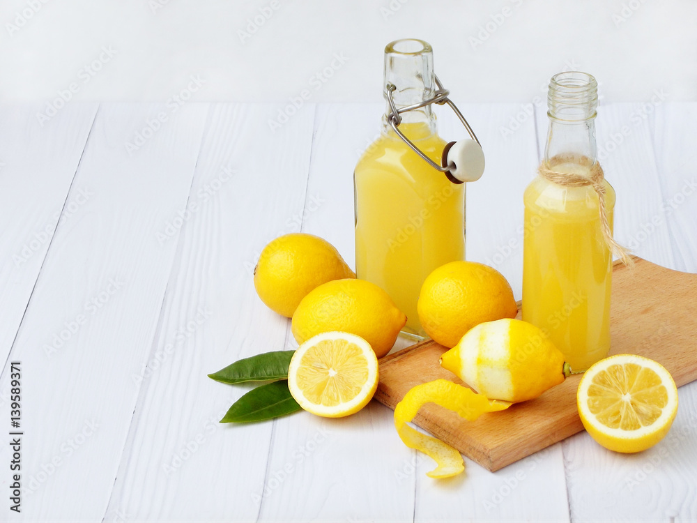 Freshly squeezed lemon juice in bottle and lemons on light background. For vitamin drink or cocktail. Selective focus. Space for text