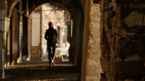 Young woman walking through the arches of the historical buildings away from the camera.