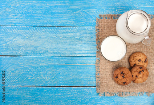 jug and glass of milk with oatmeal cookies on a blue wooden background with copy space for your text. Top view