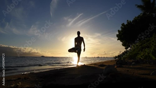 Silhouetted man doing yoga on tropical beach