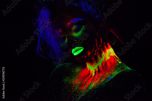 Fototapeta Naklejka Na Ścianę i Meble -  Beautiful extraterrestrial model woman with blue hair and green lips in neon light. It is portrait of beautiful model with fluorescent make-up, Art design of female posing in UV with colorful make up