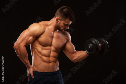 Handsome power athletic man with dumbbell confidently looking forward. Strong bodybuilder with six pack  perfect abs  shoulders  biceps  triceps and chest isolated on black background with copyspace