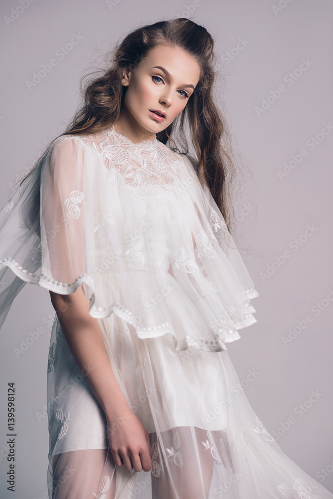 Portrait of a beautiful, gentle girl blonde in an image of the bride. Dressed in a light white lace dress. The beauty of the face. Photos in the studio on a gray background. Portrait of a beautiful, gentle girl blonde in an image of the bride. Dressed in a light white lace dress. The beauty of the face. Photos in the studio on a gray background.
