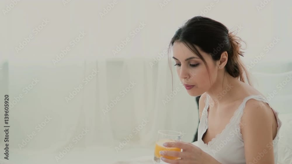 Young attractive woman drinks juice on the bed. Brunette girl surfing the Internet during breakfast, using laptop. Young attractive woman drinks juice on the bed. Brunette girl surfing the Internet during breakfast, using laptop.