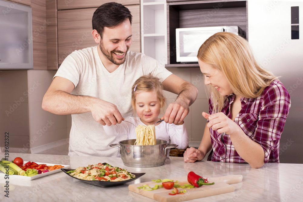 Young couple with kid having fun in kitchen while preparing spaghetti and salad Young couple with kid having fun in kitchen while preparing spaghetti and salad