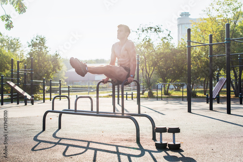 Fotografie Young strong athlete working out in outdoor gym, doing leg lifting abs exercise