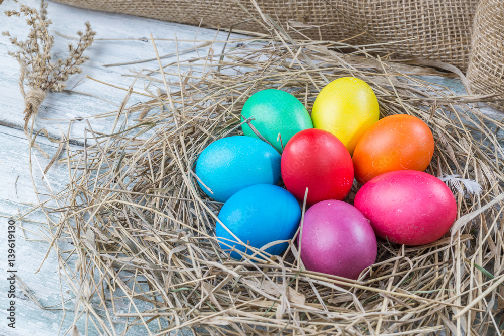 Fototapeta premium Colorful easter eggs in hay on wooden background