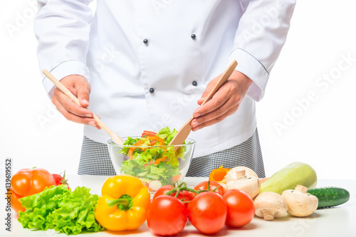 hands chef stirring with a wooden spoon vegetable salad in a bowl on a table