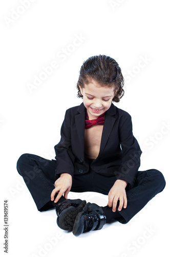 Cute little boy in a shirtless suit sits on the floor. White background.