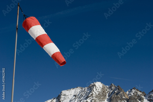 windsock red and white stripes on a sunny day in the high mountains after a snowfall, blue sky and stripes of the planes, Alps, formazza val, Italy