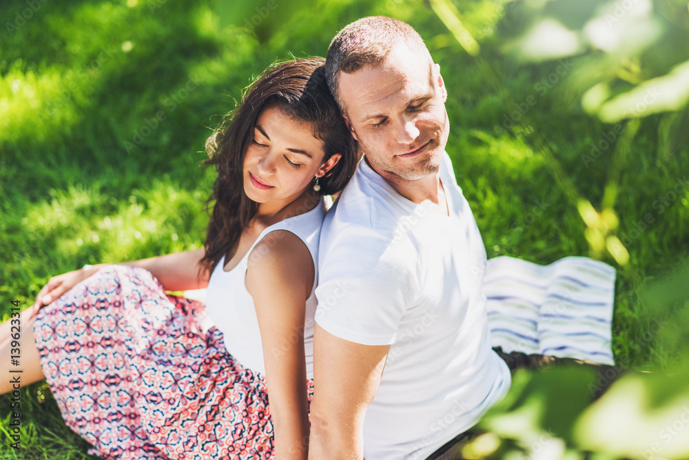 Beautiful horizontal top view of a attractive couple in love sitting on a picnic blanket. Happy caucasian dreamy man and brunette woman with closed eyes on plaid on green grass. Beautiful horizontal top view of a attractive couple in love sitting on a picnic blanket. Happy caucasian dreamy man and brunette woman with closed eyes on plaid on green grass.