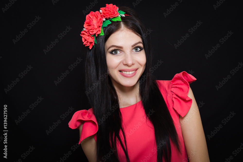 Fototapeta premium Woman with long black hair and wreath with red flowers on a dark background smiles. Close-up. Space for text