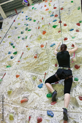 Young athletic woman practicing rock-climbing on a rock wall indoors