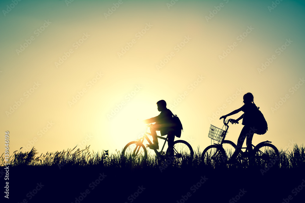 Silhouette of children with bicycle on grass field at the sky sunset, color of vintage tone and soft focus concept journey in holiday Silhouette of children with bicycle on grass field at the sky sunset, color of vintage tone and soft focus concept journey in holiday