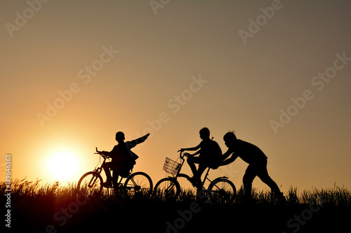 Silhouette of family with bicycle on grass field at the sky sunset, color of vintage tone and soft focus concept journey in holiday