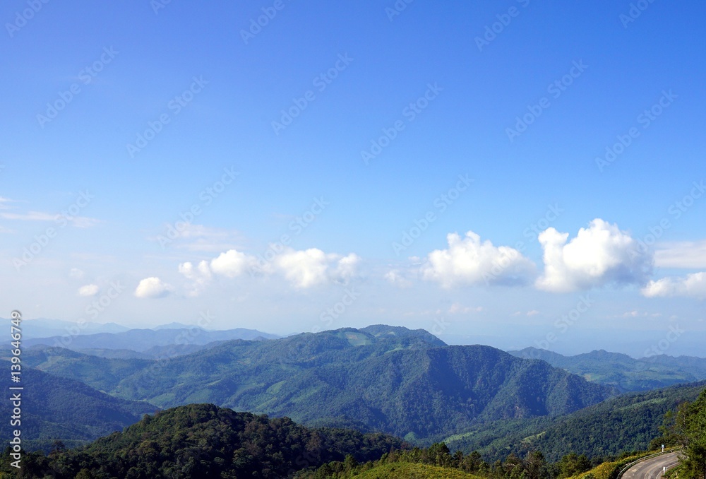 Green mountain landscape against clear blue sky with clouds and curved road at Doi Mae U-kho, Mae hong son, Thailand.