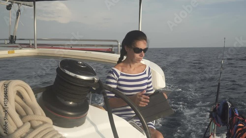 Beautiful woman in striped dress controlls the steering wheel of yacht and makes a photo photo