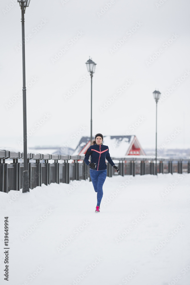 Fitness caucasian woman model running at snow winter park - sport concept
