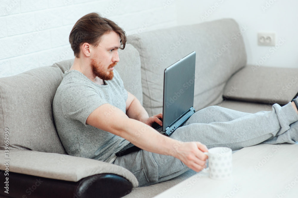 A bearded man with a laptop sitting on the sofa at home A bearded man with a laptop sitting on the sofa at home