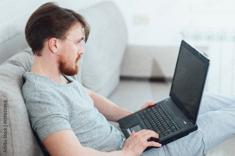 A bearded man with a laptop sitting on the sofa at home