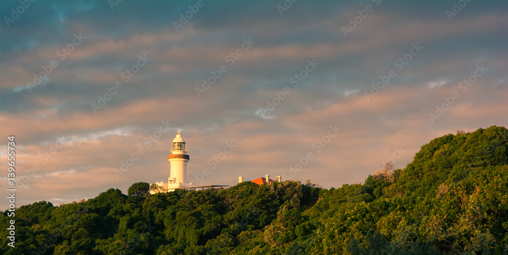 Byron Bay lighthouse view from the distance in a bright sunset light with cloudy sky, Australia