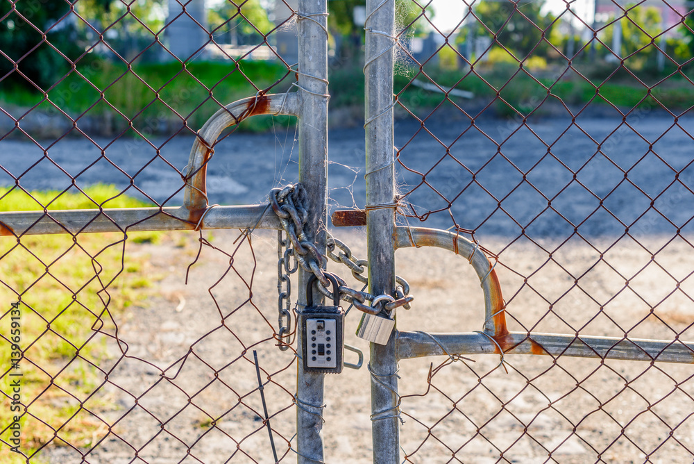 A closed and locked wire fence gate with chain and padlocks. broken and rusted A closed and locked wire fence gate with chain and padlocks. broken and rusted