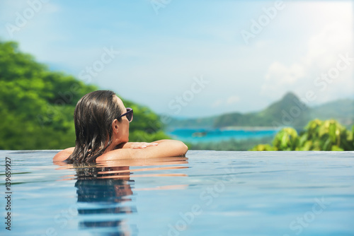 Beautiful young woman enjoying resting on the edge of outdoor swimming pool.