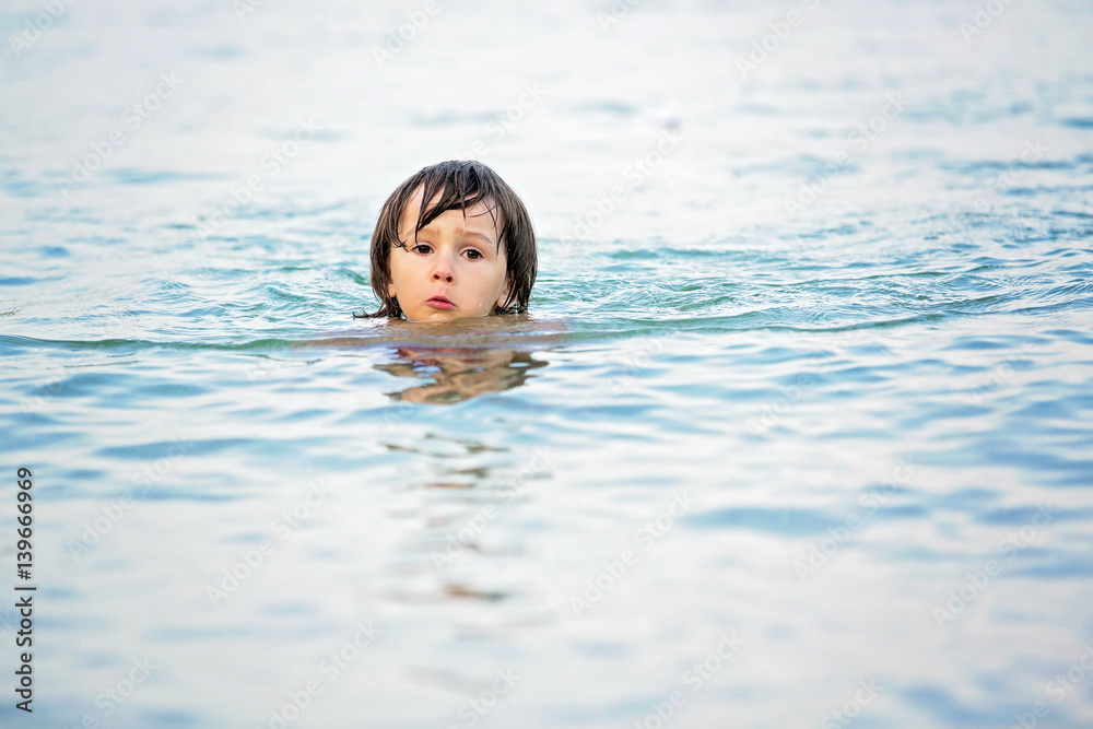 Little cute boy at the beach in the water, swimming