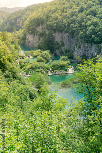 Horizontal image of tourists walking along a pathway overlooking waterfalls and lakes at Plitvice Lakes National Park in Croatia.