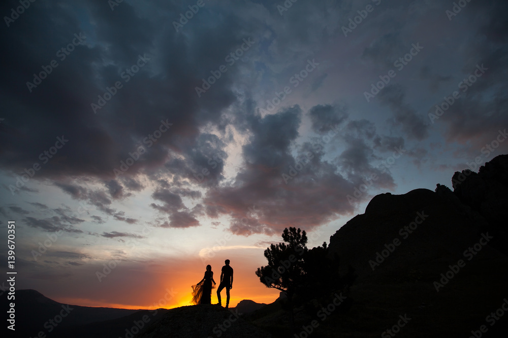 Silhouettes of a young couple lovers at sunset in rays of setting sun Silhouettes of a young couple lovers at sunset in rays of setting sun
