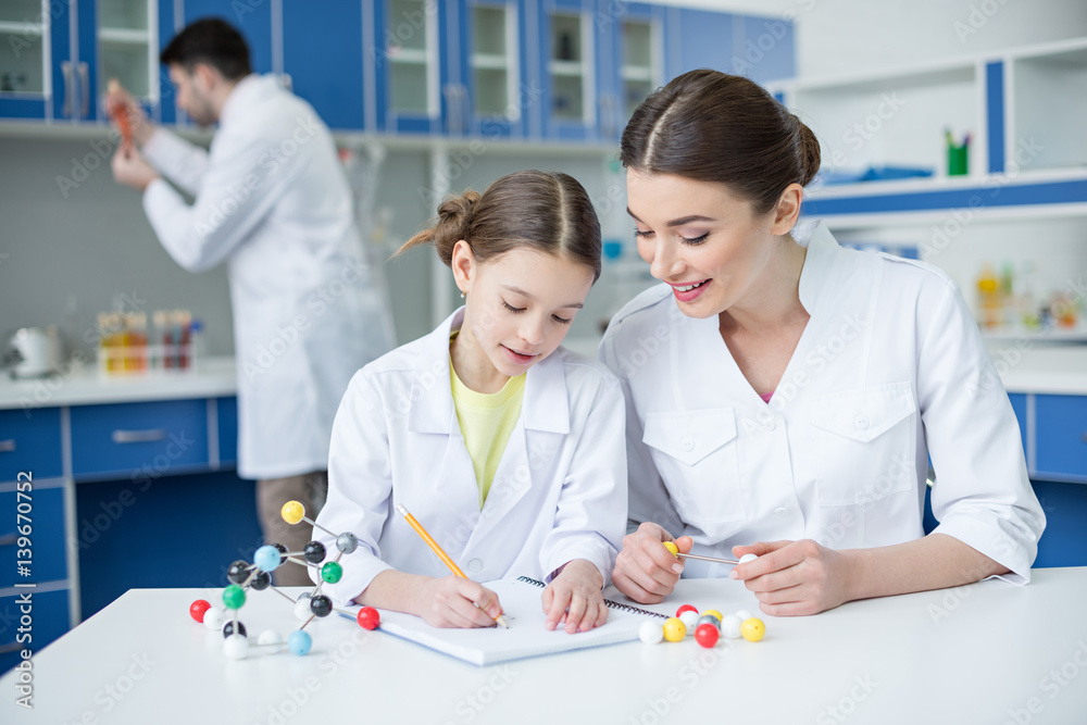 Smiling teacher and student scientists working with molecular model and taking notes Smiling teacher and student scientists working with molecular model and taking notes