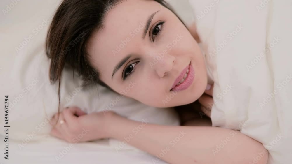 Young attractive woman lying in the bed. Girl looking at the camera and smiling. Happy woman in light room Young attractive woman lying in the bed. Girl looking at the camera and smiling. Happy woman in light room
