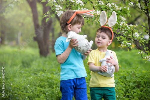 Two little kids boys and friends in Easter bunny ears during traditional egg hunt in spring garden, outdoors. Siblings having fun with finding colorful eggs. Old christian catholoc tradition photo