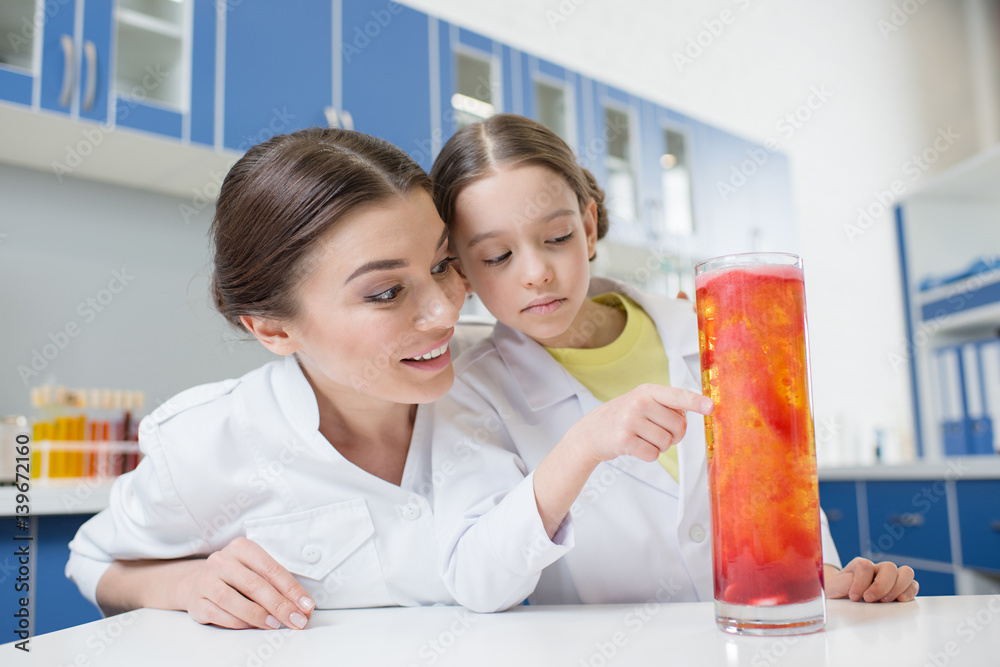 smiling woman teacher and girl student scientists analyzing experimental liquid in tube in lab smiling woman teacher and girl student scientists analyzing experimental liquid in tube in lab