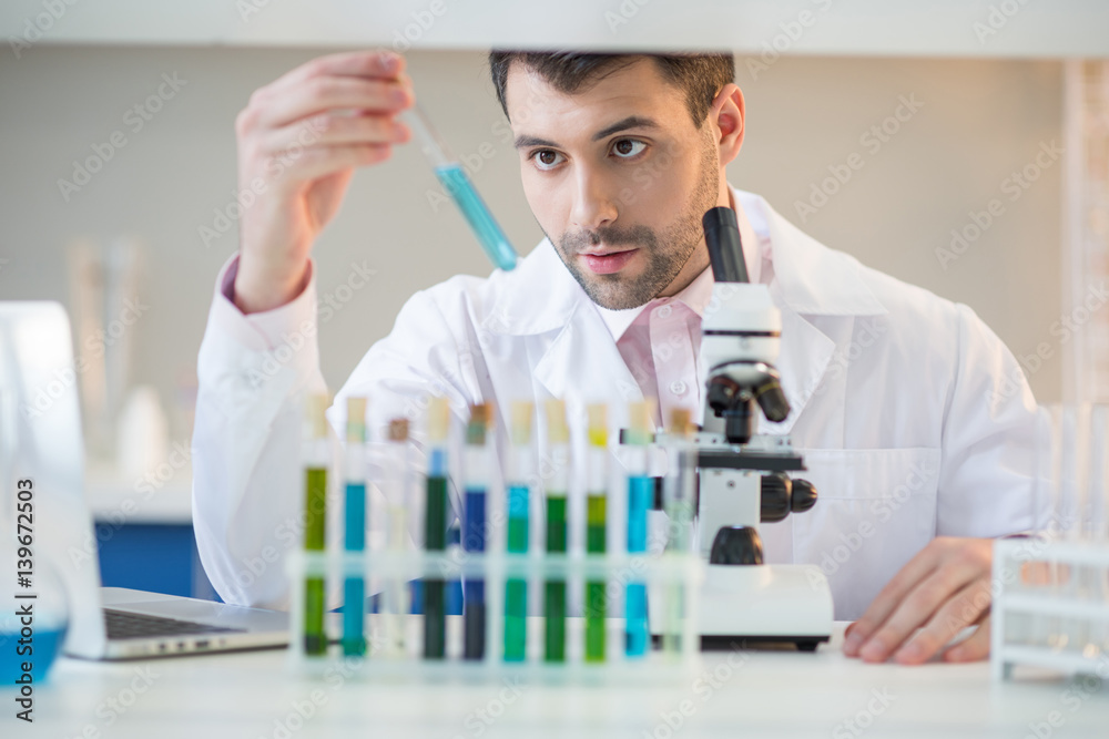 Man scientist in white coat looking at test tube with reagent in lab Man scientist in white coat looking at test tube with reagent in lab