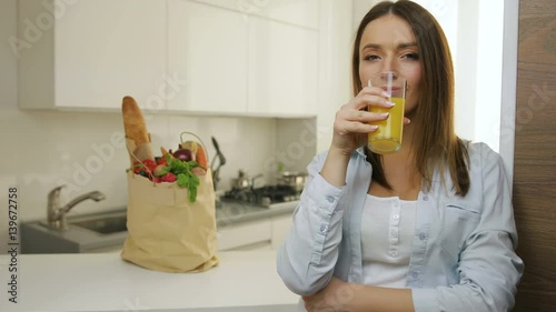 Woman drinking orange juice in the kitchen.