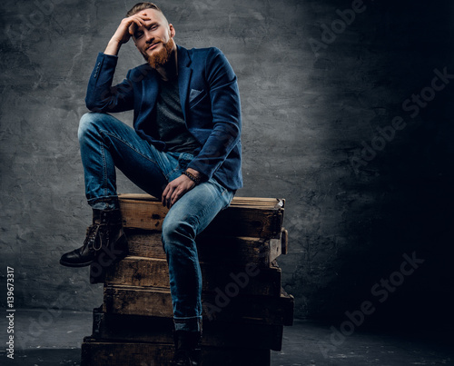 Redhead male dressed in a jeans and a shirt posing on a wooden box.
