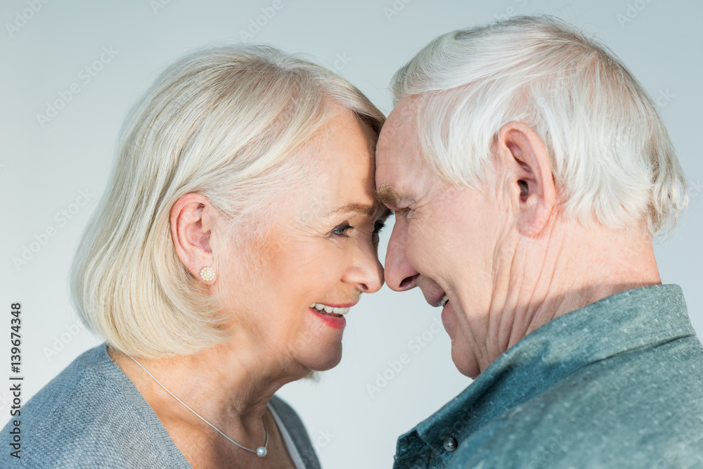 side view of smiling senior man and woman looking at each other on grey side view of smiling senior man and woman looking at each other on grey