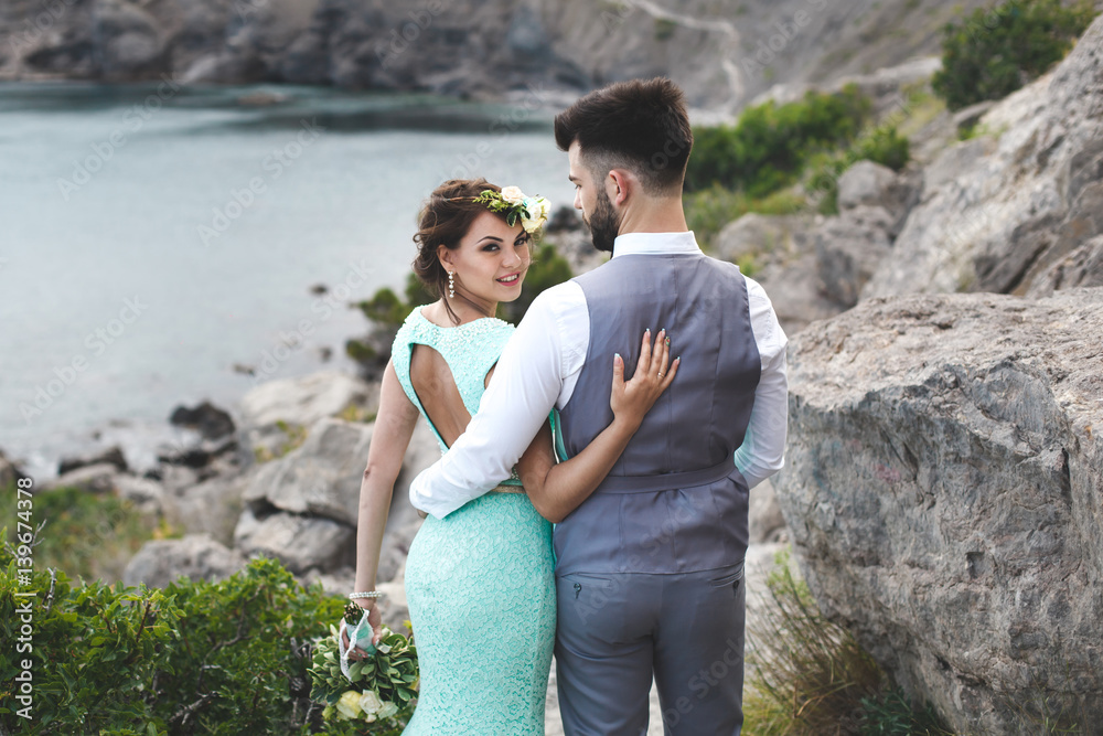 The bride and groom on nature in the mountains near the water. Suit and dress color Tiffany. Walk hand in hand.