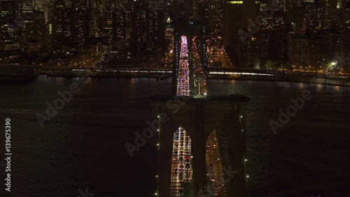 AERIAL HELI SHOT, NO VISIBLE TRADEMARKS Automobile traffic moving across the iconic Brooklyn bridge lit up with lights on magical summer night in New York City. People commuting from work at rush hour