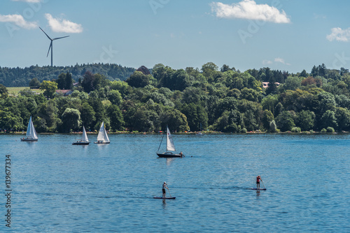 Starnberger See mit Stehpaddlern und Segelbooten und einem Windrad