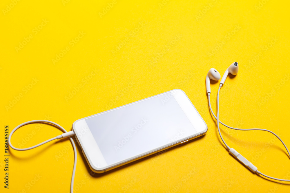 Obraz premium Close-up of smart phone with headphones on a yellow background. (Top view). Listen to music